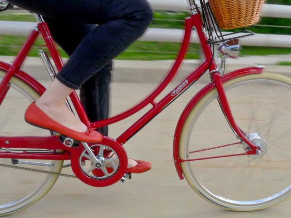 legs of a bicyclist wearing blue jeans and red shoes, pedaling a red bike.